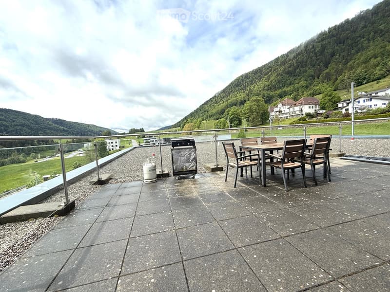 Balcony with a table, chairs, and a grill, overlooking a scenic mountainous landscape.