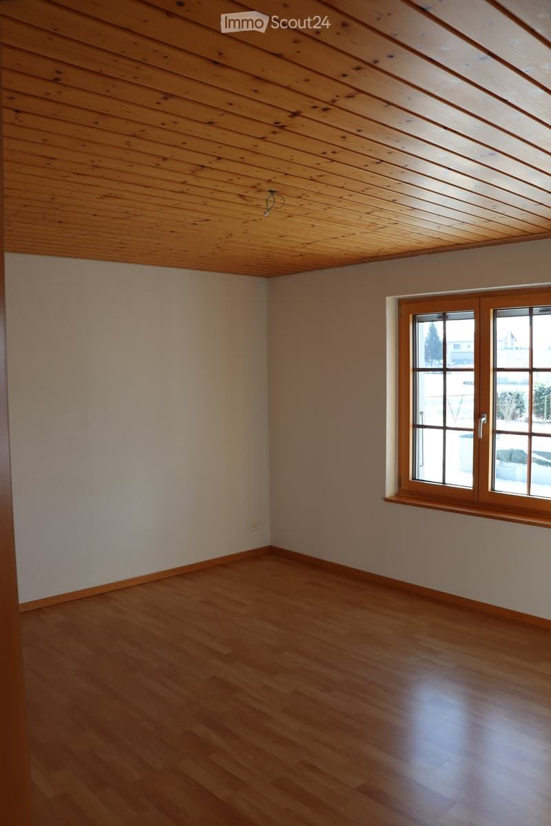 Empty room with wooden floor, light-colored walls, and a large window with wooden frame and sill.