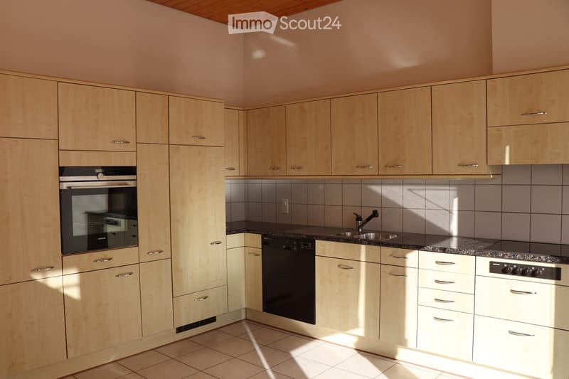 Modern kitchen with light wooden cabinets, stainless steel appliances, and granite countertop.