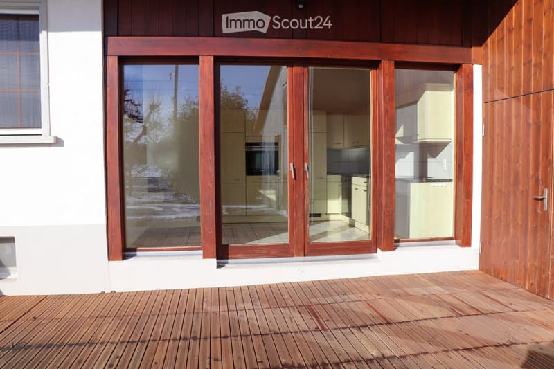 Wooden deck with large glass sliding doors leading to a modern kitchen interior.