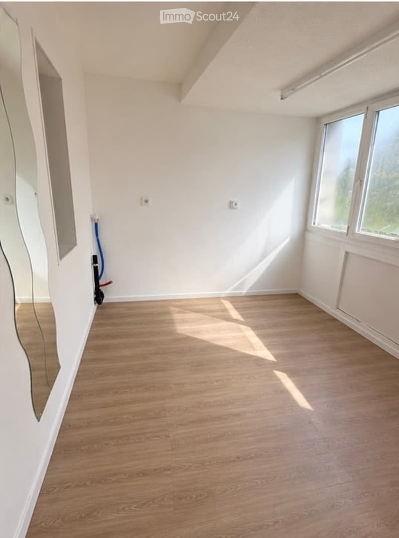 Empty room with light wooden flooring, white walls, and large windows allowing natural light. No furniture or equipment present.