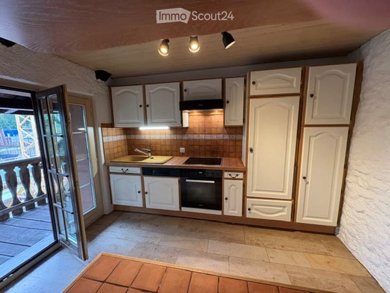 Bright kitchen with white cabinets, a sink, stove, and oven. Features a large window with a view to a balcony.