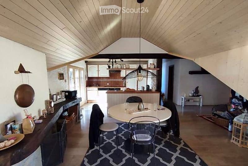 Open-plan living and dining area with a dining table and chairs, kitchen area with cabinets and appliances, and a fireplace with decorative items.