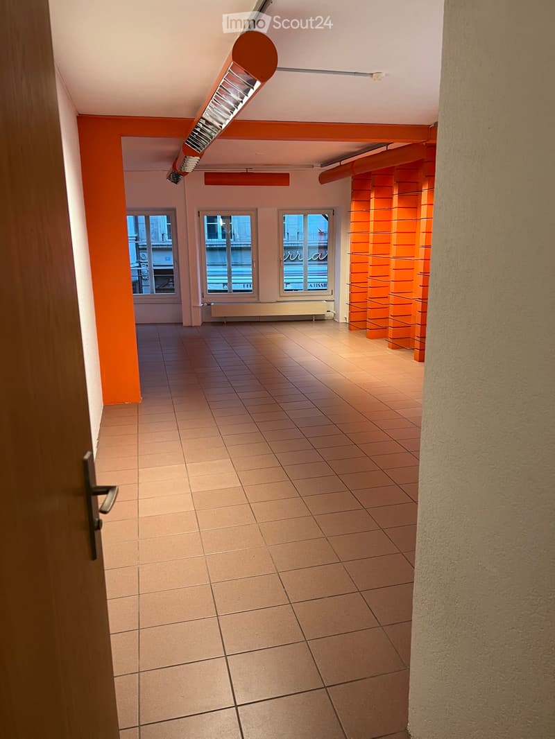 Empty hallway with tiled floor, orange accent wall, and three windows at the end.