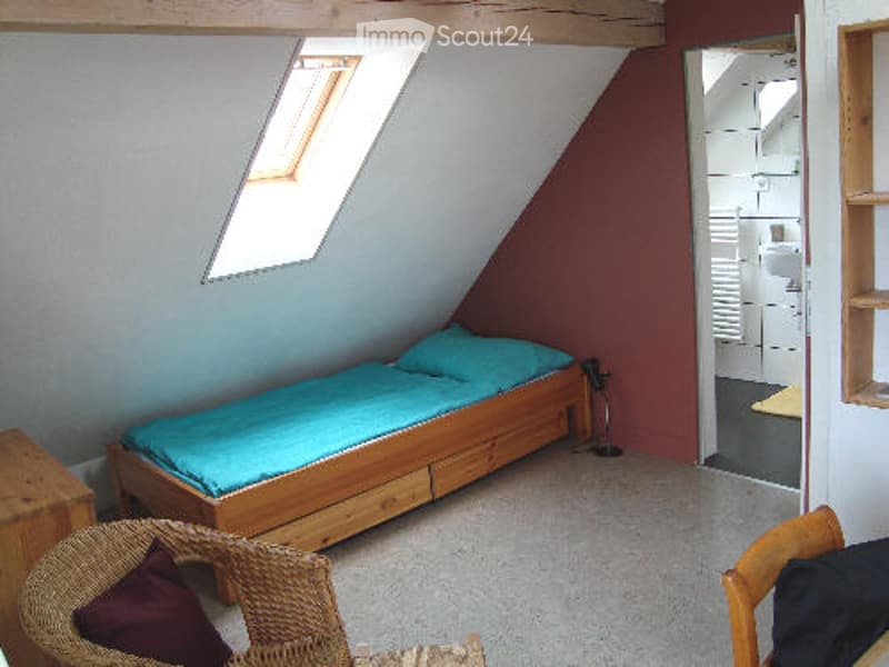 single bed with blue blanket and pillow, wooden chair, small wooden nightstand, small window, small closet