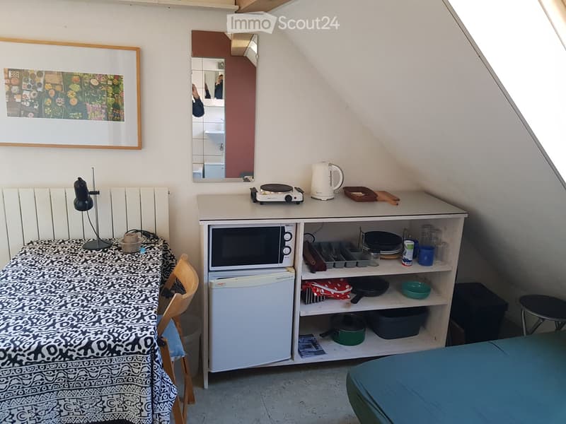 small attic room with a desk, chair, microwave, refrigerator, and a bed.