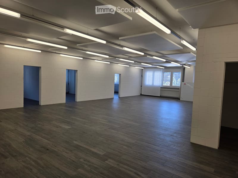 Empty room with wooden flooring, white brick walls, and exposed ceiling beams. Features multiple doors and windows with blinds.