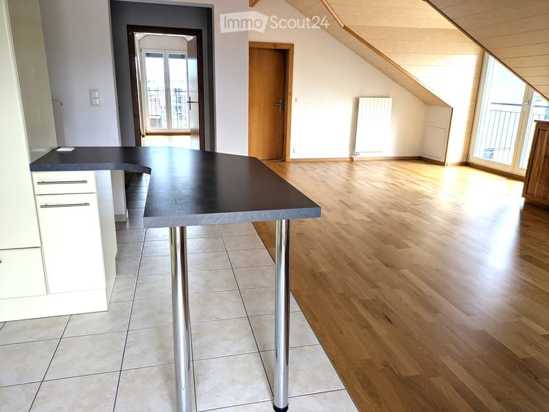 Modern kitchen with a black countertop table, white cabinets, and wooden flooring. The room features large windows and a door leading to a balcony.