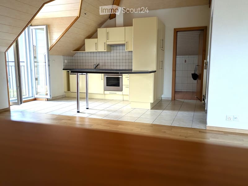 Bright kitchen with light-colored cabinets, a black countertop, and a small table. The room features wooden flooring and a large window with blinds.