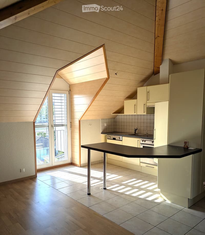 Bright kitchen with wooden ceiling beams, white cabinets, a central island with a black countertop, and a large window offering a view of the garden.