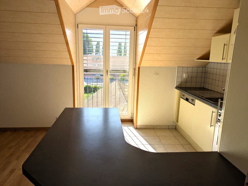 Modern kitchen with a black countertop, white cabinets, and a stove. The room features wooden flooring and large windows with blinds, allowing natural light to fill the space.