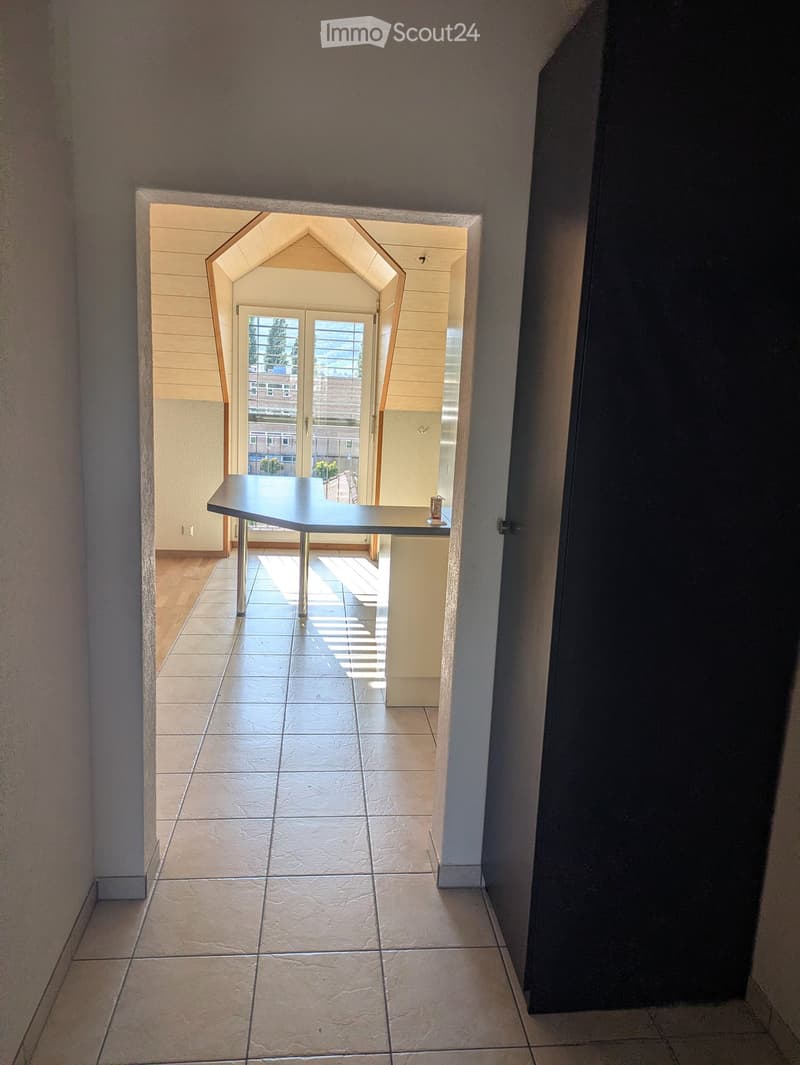 A clean, tiled hallway with a modern, arched doorway leading to a room with a small table and a view of the outside. The walls are painted in neutral tones, and the floor is made of large, light-colored tiles.