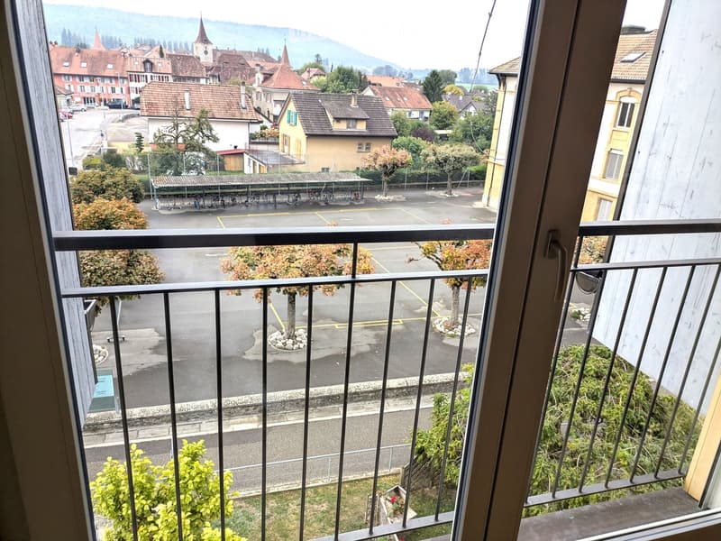 Balcony overlooking a parking lot and town with trees, buildings, and distant mountains.