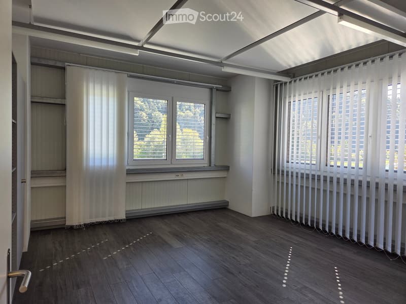 Empty room with wooden flooring, white walls, large windows with blinds, and a door. No furniture or equipment present.