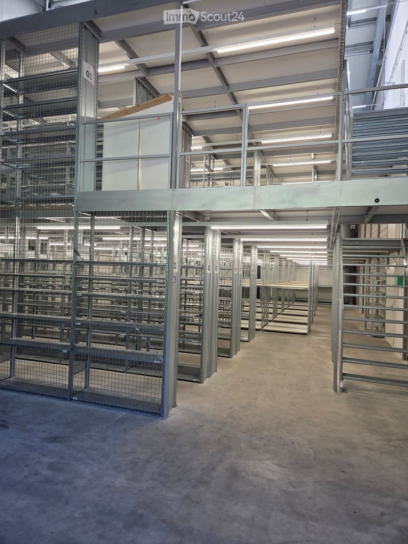 Large industrial-style warehouse with metal shelving units, concrete floor, and exposed steel beams and lighting fixtures.