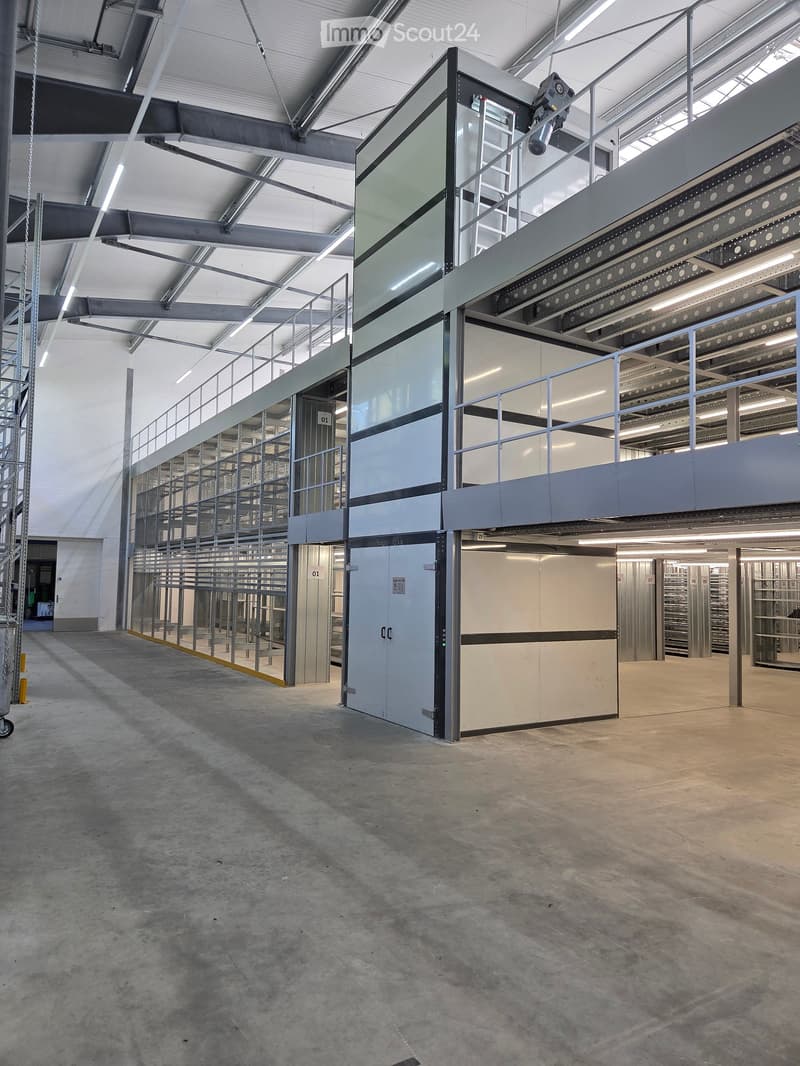 Empty industrial-style room with concrete floors, metal shelving units, and a raised platform with glass walls and railings.