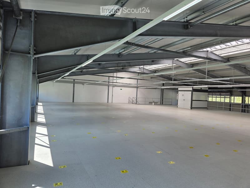 Empty industrial-style room with concrete floors, exposed metal beams, and fluorescent lighting. No furniture or equipment present.