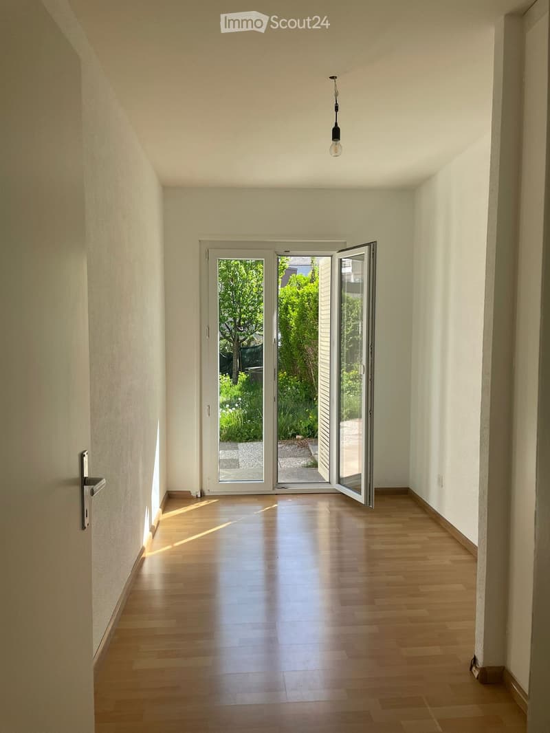 Bright hallway with wooden flooring, white walls, and a large open door leading to a garden area.