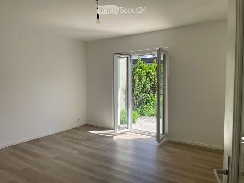 Empty room with wooden flooring, white walls, and large sliding glass doors leading to a garden area.