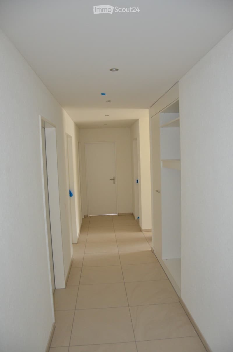 Empty hallway with tiled floor, white walls, and several doors leading to rooms.