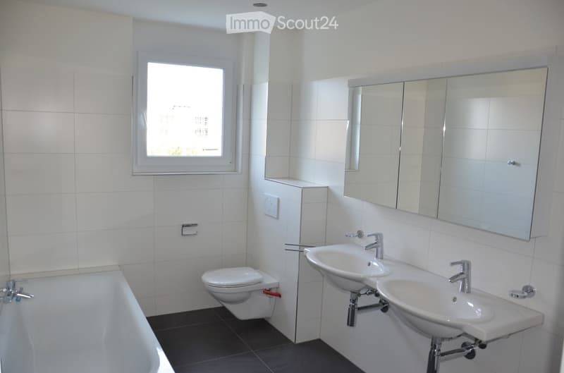 Modern bathroom with white tiles, a bathtub, toilet, double sink, and large mirror.