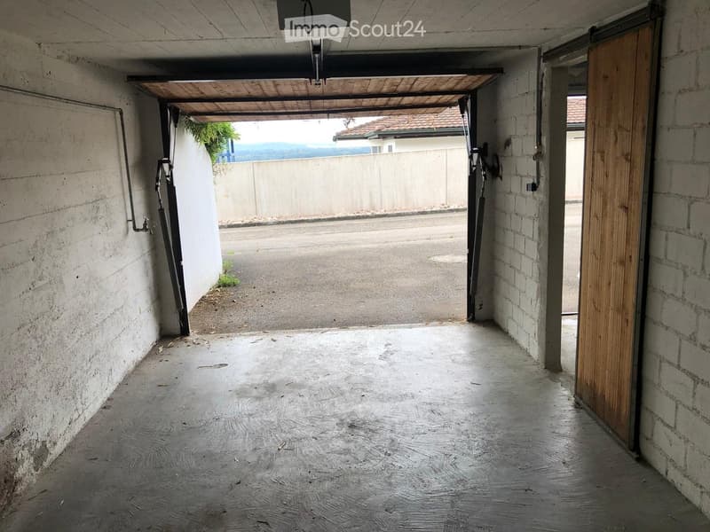 Empty covered corridor with concrete walls, wooden door, and open view to the outside.