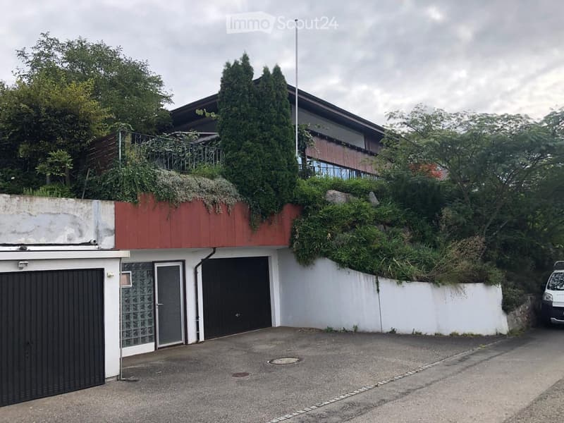 Two-story house with a red roof, white walls, garage, and greenery on the roof.