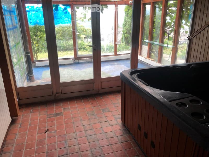 Empty room with red tiled floor, large glass doors leading to an outdoor area, and a black sink unit on the right side.