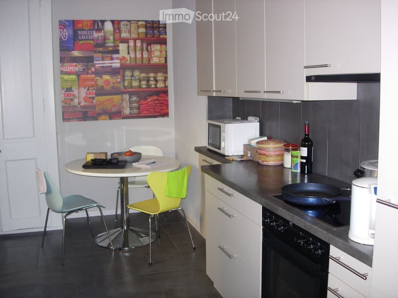 Modern kitchen with white cabinets, dark countertops, and a small dining area featuring a round table and colorful chairs.