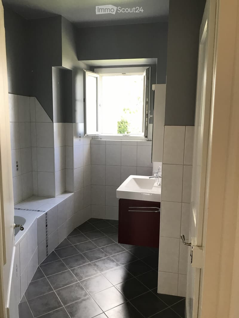 Modern bathroom with a white sink, dark grey tiles, and a large window letting in natural light.