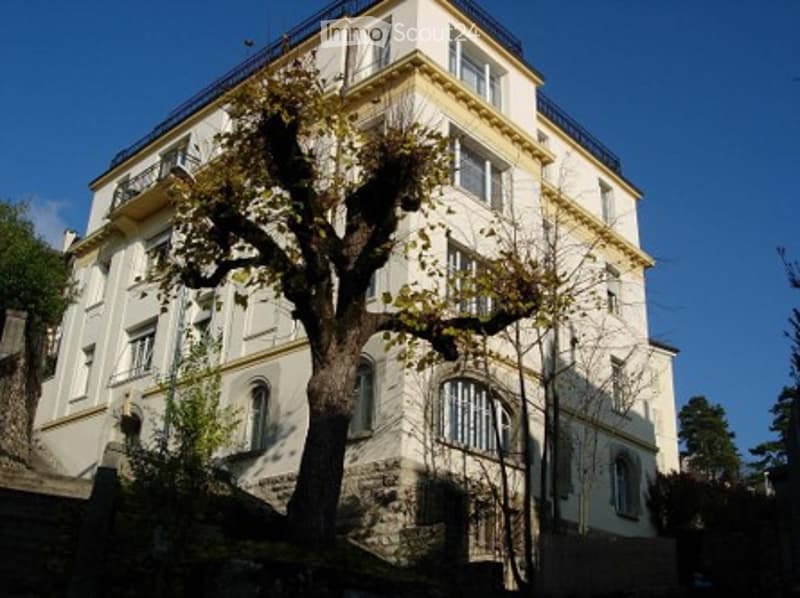 A multi-story building with a balcony on the top floor, surrounded by trees.