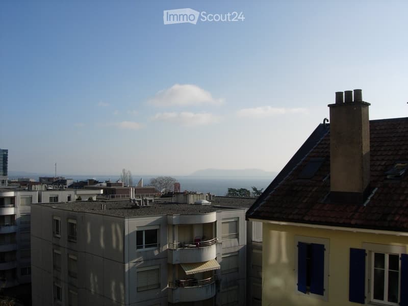 View of a multi-story residential building with balconies and a distant cityscape and sea view.