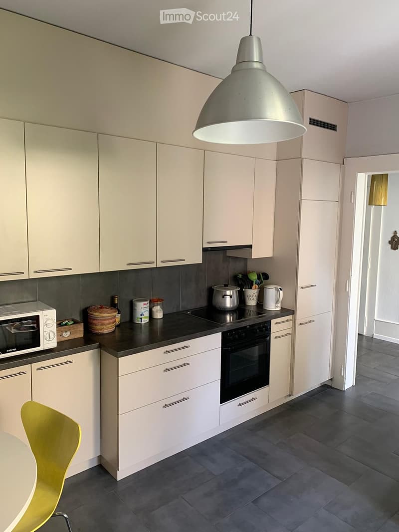 Modern kitchen with white cabinets, black countertops, and stainless steel appliances. Includes a microwave, oven, pot, cup, and a yellow chair.