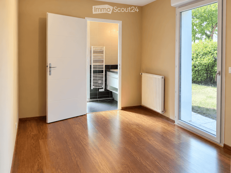 Empty room with wooden flooring, white walls, a sliding glass door leading to a garden, and a radiator on the wall.