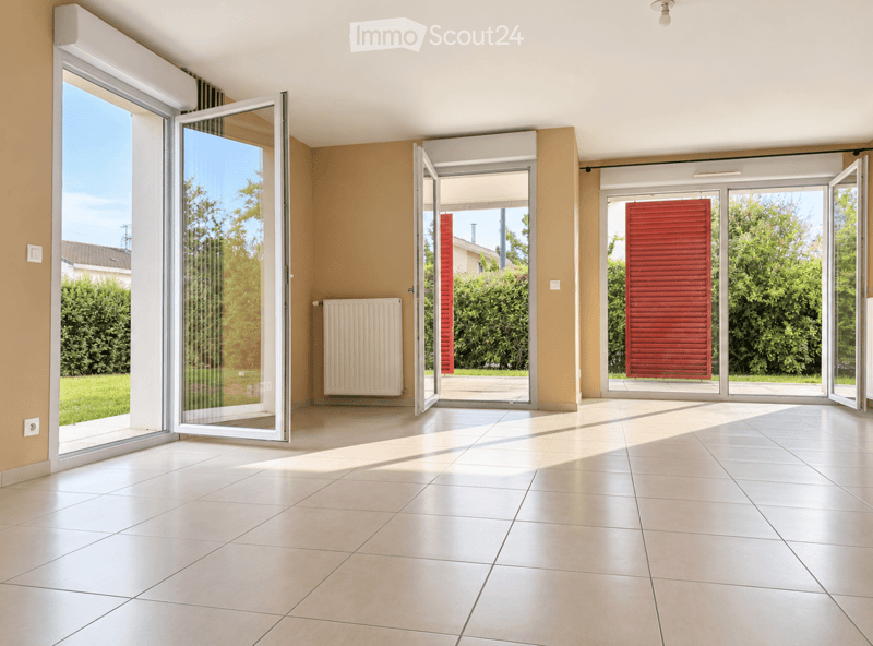 Empty room with large sliding glass doors leading to an outdoor area, tiled floor, radiator, and visible outdoor greenery.