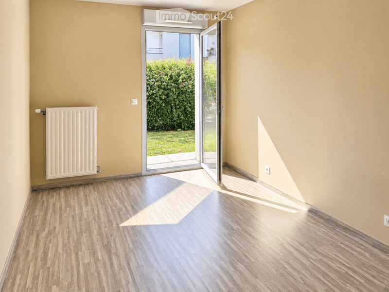 Empty room with light yellow walls, wooden flooring, and a white radiator on one wall. A large sliding glass door opens to a green garden area.