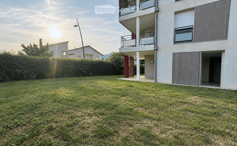 Lush green lawn in front of a modern multi-story building with balconies and wooden shutters.