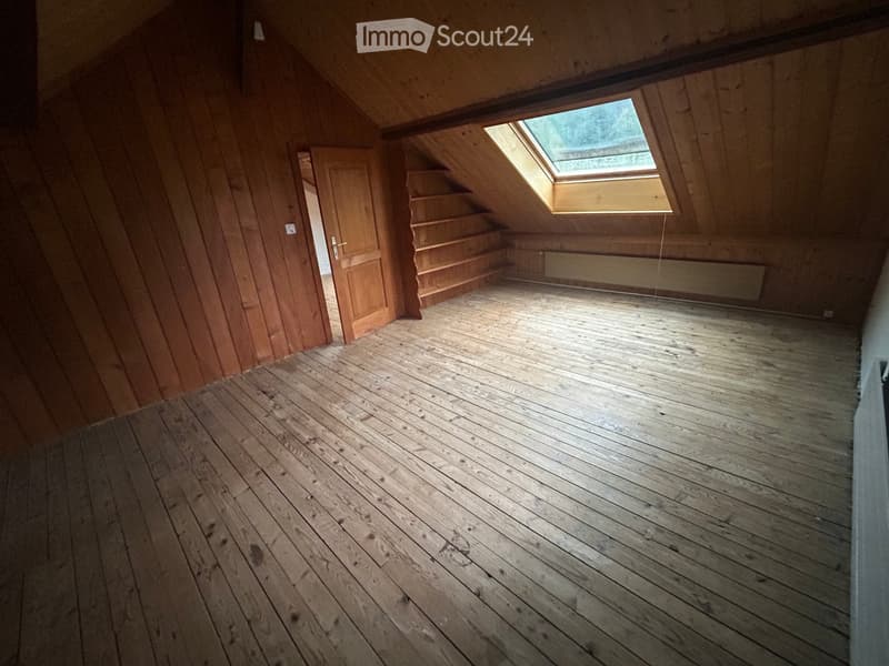 Empty attic space with wooden walls, wooden floor, skylight window, and a small staircase leading to another area.