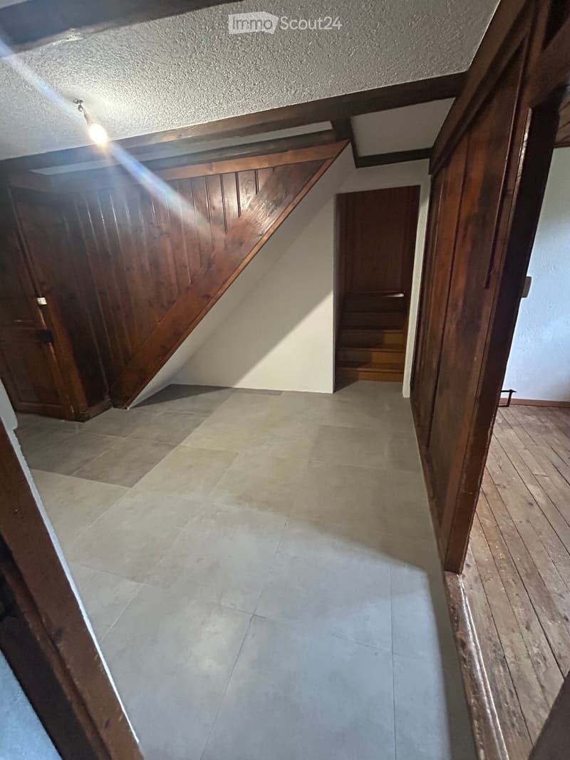 A narrow hallway with tiled floor, wooden walls, and a staircase leading upwards.