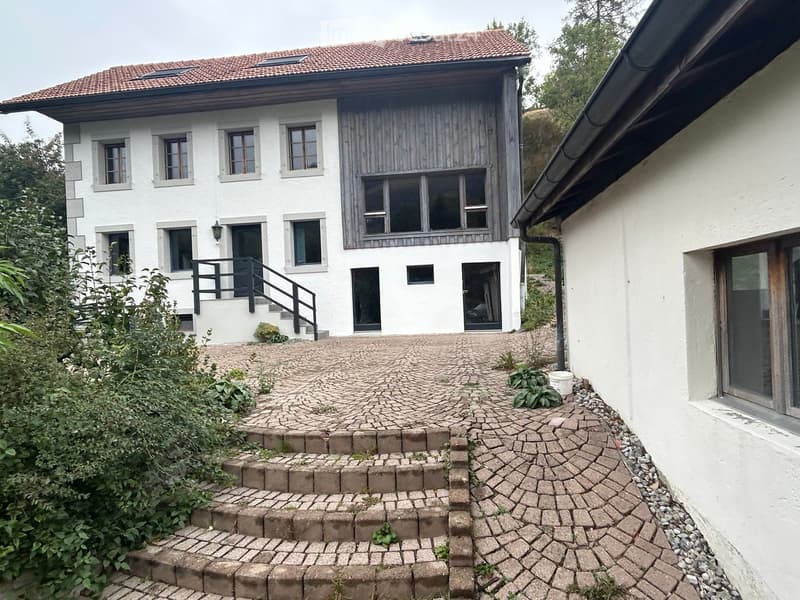 Two-story house with white exterior, red-tiled roof, multiple windows, and a raised ground floor accessed by steps.