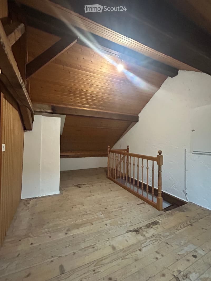 Empty attic space with wooden floor, slanted wooden ceiling, and a small wooden staircase leading to another level.