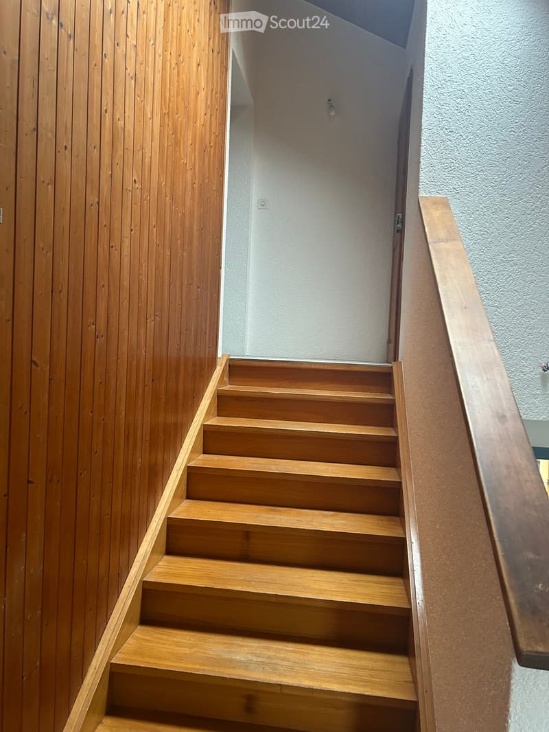 Wooden staircase with a handrail, light-colored walls, and a small open area at the top.