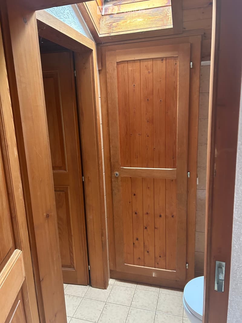 Bathroom with wooden doors, tiled floor, and a toilet visible in the corner.