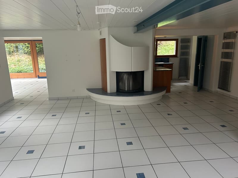 Empty living room with tiled floor, white walls, and a modern fireplace. There are large windows and doors leading to an outdoor area.