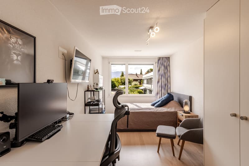 A modern bedroom with a bed, a desk setup, and a large window offering a scenic view. The room features a sleek design with contemporary furniture and decor.