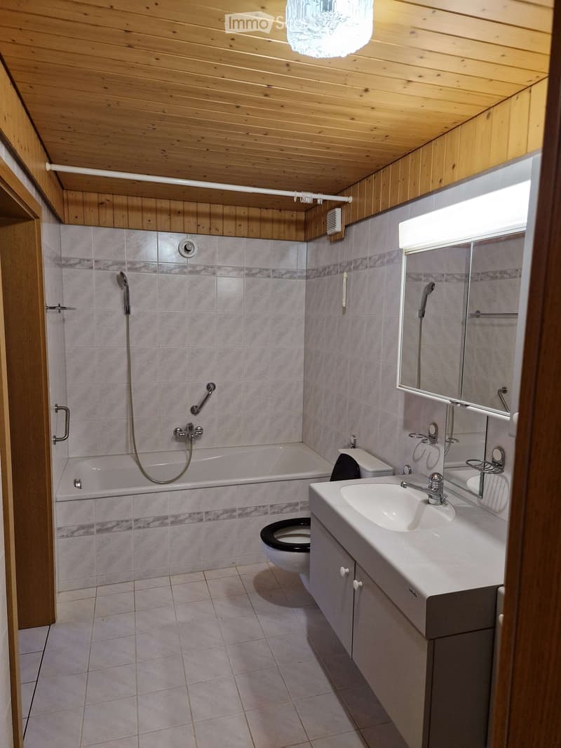 Bathroom with wooden ceiling and walls, tiled shower area, bathtub, toilet, sink, and mirror.