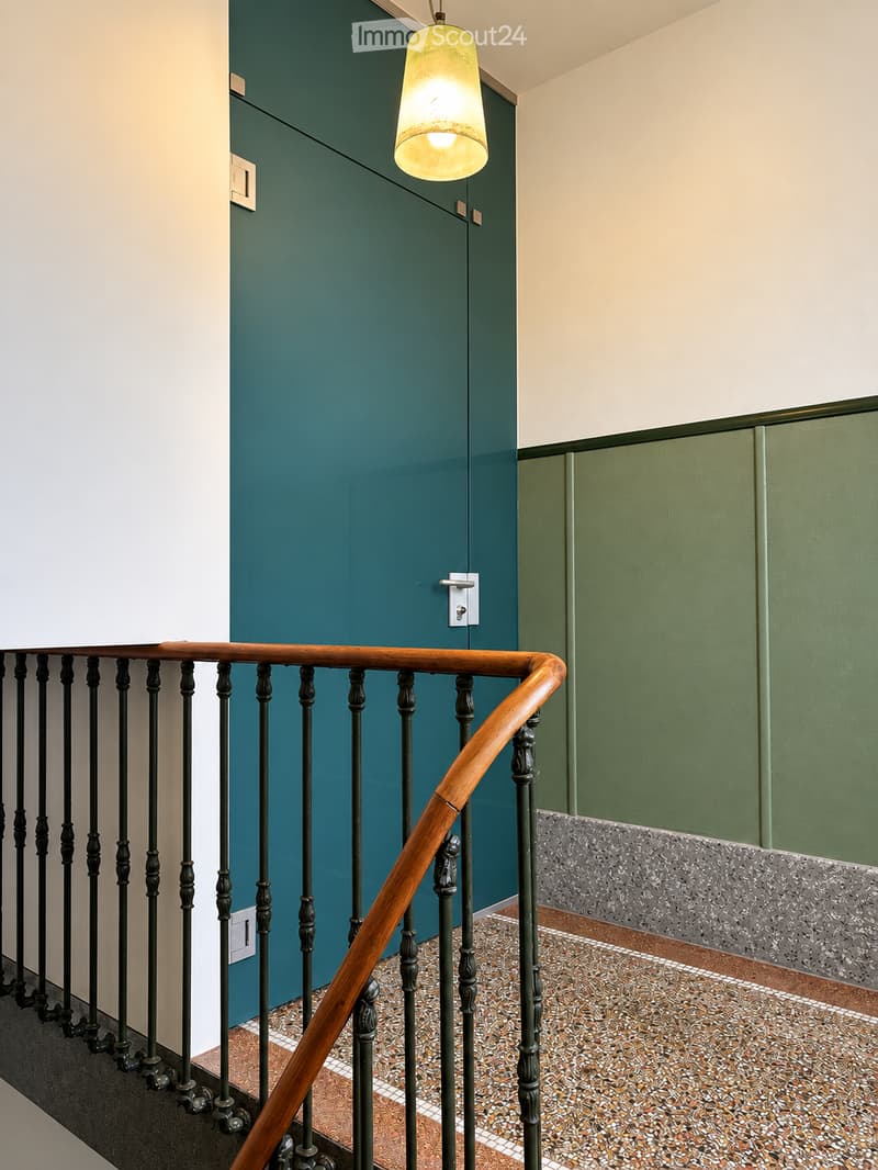 Staircase with wooden handrail and metal balusters, teal and green walls, pendant light fixture, and patterned tile flooring.
