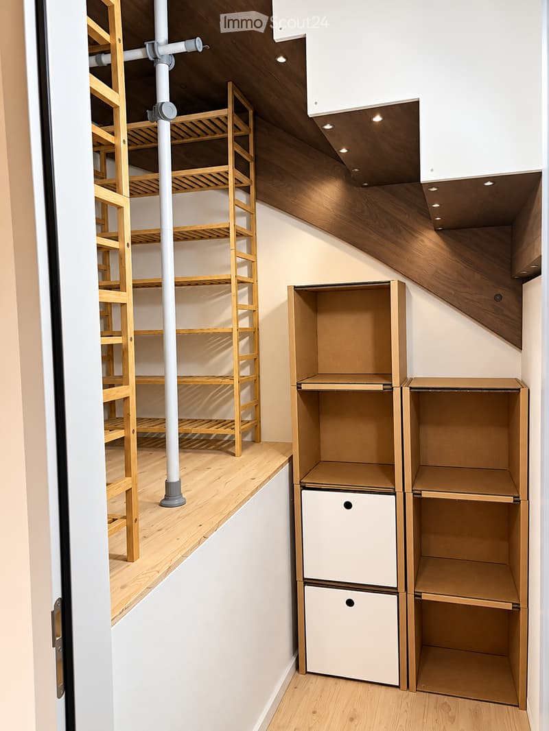 The image shows an empty, modern storage room with wooden shelves and cabinets, white walls, and recessed lighting. The room is unfurnished and contains no visible furniture or personal items.