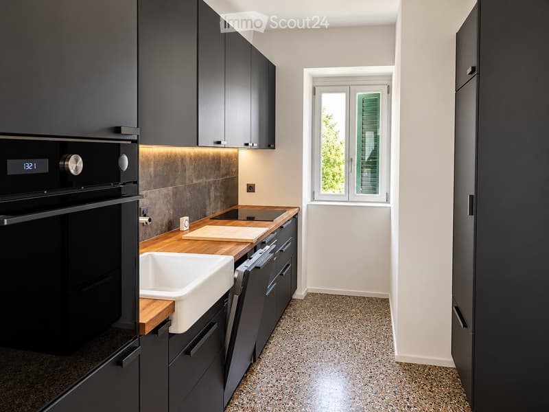 Modern kitchen with dark grey cabinets, a white sink, wooden countertop, and built-in oven and dishwasher.