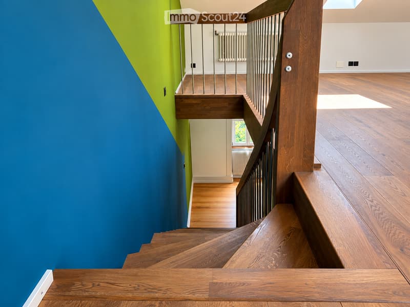 Staircase with wooden steps and railings, blue and green accent wall, wooden flooring, visible room in the background with radiator and window.